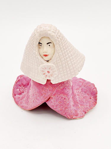 Cloaked person in pink with a ivory head covering